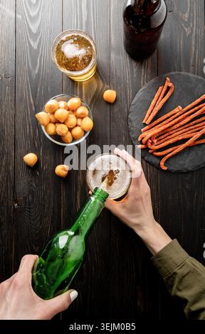Top view of beer pouring from bottle into glass, black wooden background Stock Photo