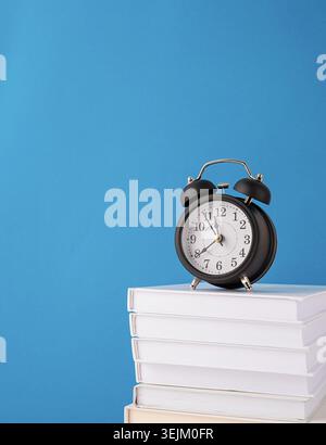 Black alarm clock on stack of books on blue background, mockup design Stock Photo