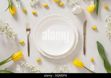 Easter table setting with yellow tulips, white plate, eggs and bunny. Stock Photo