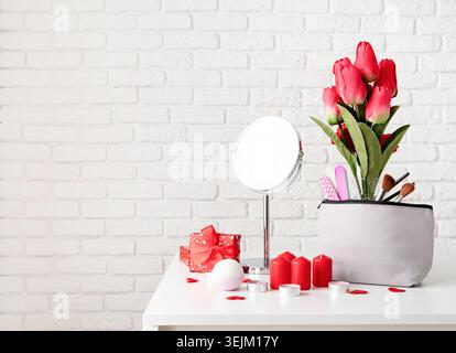 Cosmetic and spa accessories with gift box, flowers and candles on dressing table front view on white brick wall background with Stock Photo