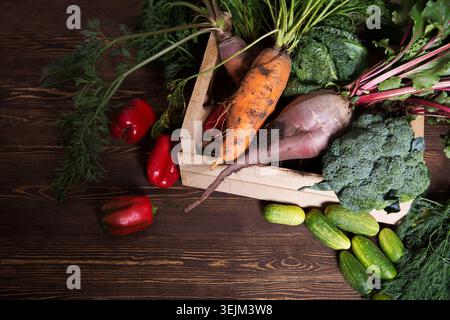 A box of fresh garden Organic vegetables peppers, cucumbers, beets, carrots, broccoli, greens on a wooden table. Overhead shop Stock Photo