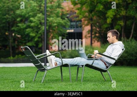 Millennial web developer work outside in urban park using laptop and smartphone. Distant workspace Stock Photo