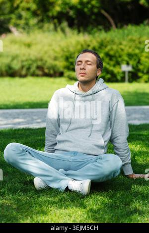 Freelancer man sitting on grass in park resting during break from work, relaxed, breathes fresh air Stock Photo