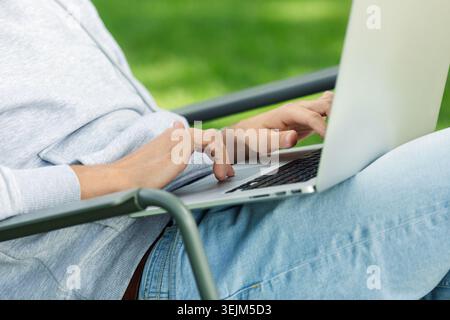 Close up arms of blogger man with laptop working outdoors in garden, sitting on chair. Stock Photo
