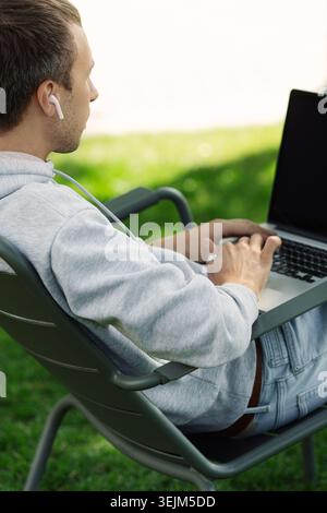 Blogger male work on computer in public park processes video for social media content. Distance job. Stock Photo