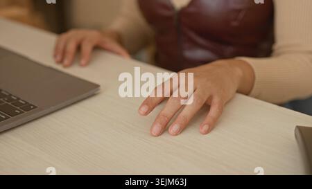 Woman hand hovering over light wood desk beside laptop in studio, fingers slightly splayed and poised above surface; focused productivity. Stock Photo