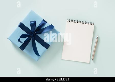 Blue gift box, spiral notebook and pen on blue. View from above. Stock Photo