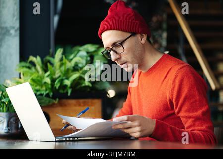 Serious freelancer man in glasses remote work with laptop sitting in coworking working with document Stock Photo