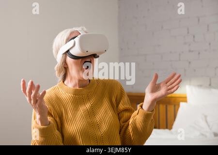 Virtual reality. VR, future, gadgets. senior woman playing game in virtual reality glasses and holds joysticks at home Stock Photo