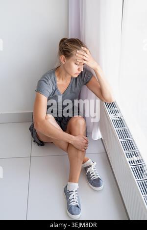 Sad woman sitting on the floor hugging her knees Stock Photo
