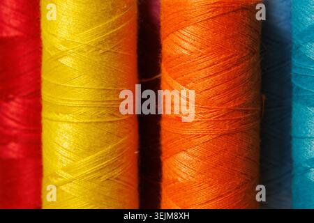 Colorful Sewing Thread Spools Standing in a Row on Wooden Surface Stock Photo