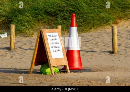 A wooden A-frame sandwich board sign reading "The beach carpark gates will be locked at 8:30pm" at Ainsdale beach, Ainsdale, UK/ Stock Photo