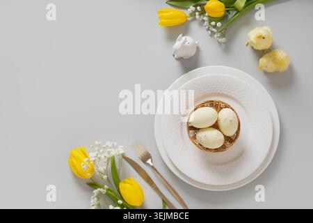 Easter table setting with yellow tulips, white plate, eggs and bunny. Stock Photo