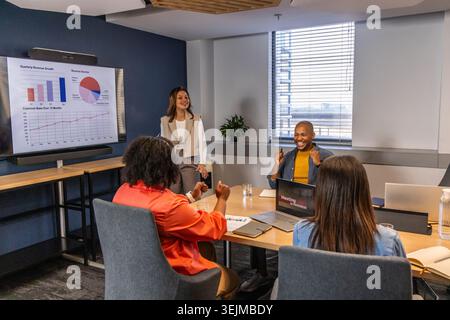 Diverse coworkers presenting and discussing charts on large monitor in conference room with laptops. Graphs, display, team, coll Stock Photo