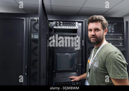 IT technician working in a data center server room checking rack equipment and network systems Stock Photo