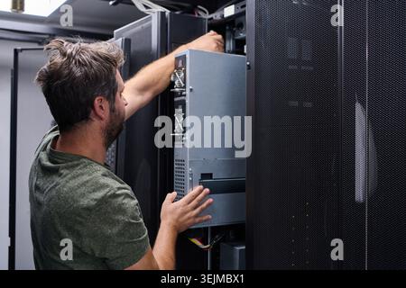 IT technician works inside a data center rack performing server maintenance and hardware installation. The image conveys technical expertise, precisio Stock Photo
