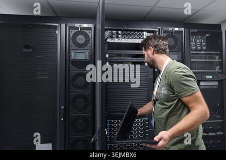 IT technician inspecting server rack in a data center with laptop during maintenance Stock Photo