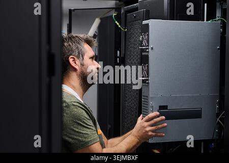 IT technician installing server hardware in a data center server rack performing maintenance and equipment check Stock Photo