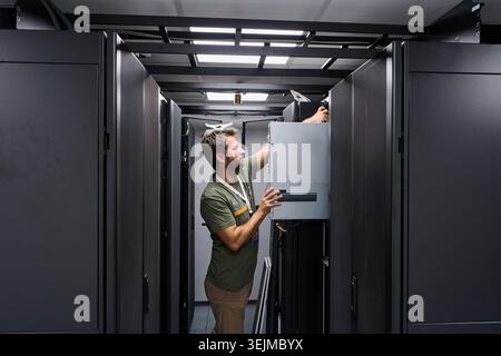 IT technician installing server hardware in a data center server rack maintenance environment Stock Photo