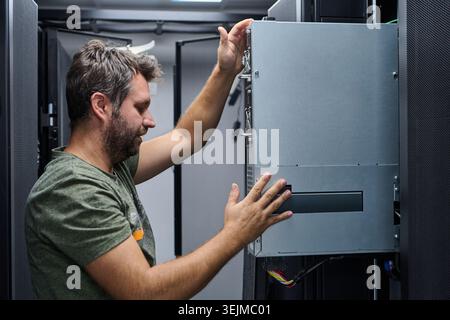 IT technician working inside a data center, installing and adjusting server hardware in a rack while performing maintenance, cable management and netw Stock Photo
