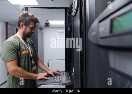 IT technician configuring servers on a rack console in a data center server room Stock Photo