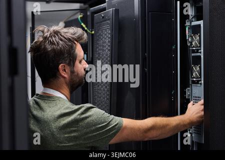 IT technician working in a server room, inspecting equipment and performing maintenance on server racks and network hardware to ensure uptime, connect Stock Photo