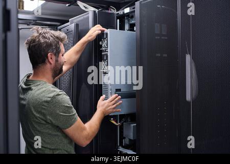 Server technician installing a rack server in a modern data center performing IT maintenance and hardware upgrade Stock Photo