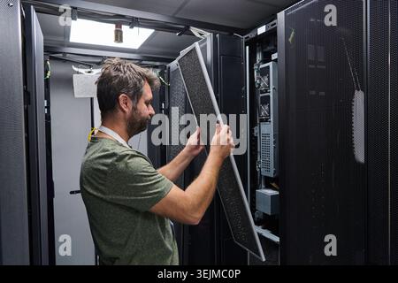 IT technician performing server maintenance in a data center rack replacing air filter panel Stock Photo