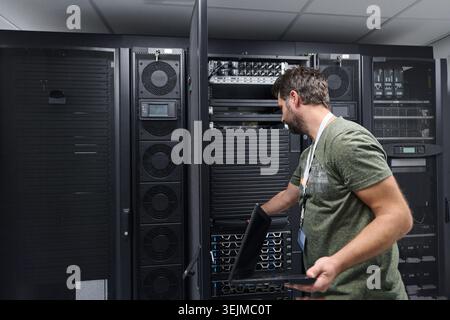 IT technician working on servers in a data center with laptop performing maintenance and monitoring Stock Photo