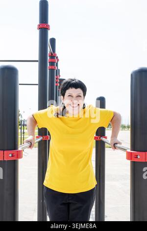 Smiling senior woman doing reverse push ups outdoors on the sports ground bars Stock Photo