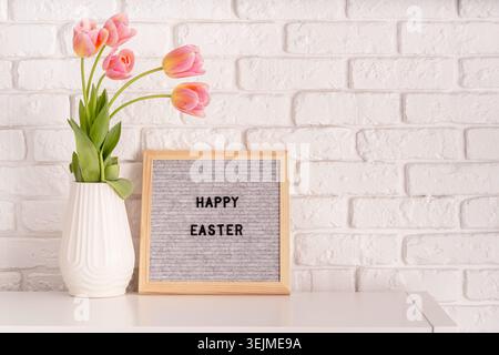 Vase with tulips and gray felt letter board with words Happy Easter on white bricks background Stock Photo