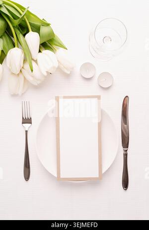 Mock up menu frame in restaurant or cafe. Top view of table setting with menu card, cutlery, fresh white tulips, wine glass and Stock Photo
