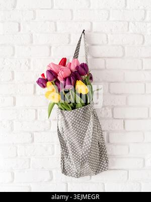 Gray polka dot fabric bag full of colorful tulips on white brick background Stock Photo