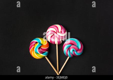 Color lollipop, spiral candy on stick, colorful striped lollypop, round fruit caramel, multicolored confectionery, circle lollipop on black background Stock Photo