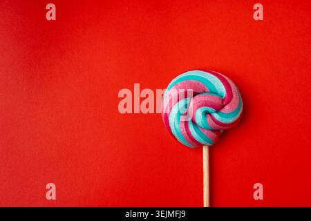 Color lollipop, spiral candy on stick, colorful striped lollypop, round fruit caramel, multicolored confectionery, circle lollipop on red background, Stock Photo