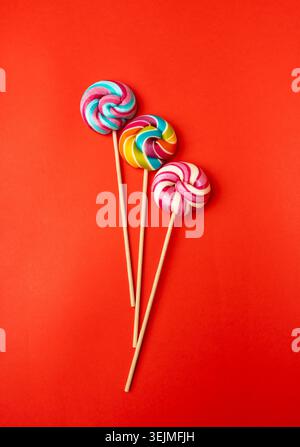 Color lollipop, spiral candy on stick, colorful striped lollypop, round fruit caramel, multicolored confectionery, circle lollipop on red background, Stock Photo