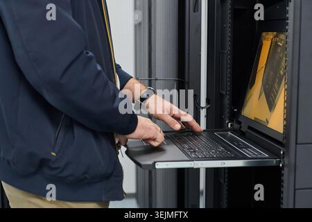 Data center technician using laptop on rack-mounted console to manage servers and network equipment Stock Photo
