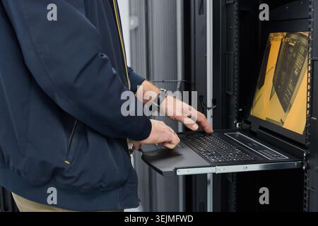 IT technician using a rack-mounted laptop to monitor servers during maintenance in a data center Stock Photo