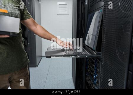 IT technician using a rack-mounted laptop console to maintain servers in a data center, monitoring hardware and performing configuration and diagnosti Stock Photo