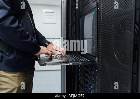 IT technician working on laptop in server rack during data center maintenance and network troubleshooting Stock Photo