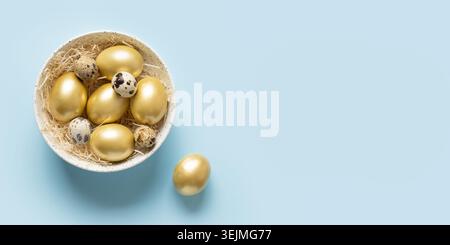 Easter banner with golden chicken eggs in bowl on blue. View from above. Stock Photo