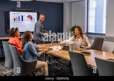 Diverse team in business attire meeting in conference room handing reports while discussing charts. Office, boardroom, collabora Stock Photo