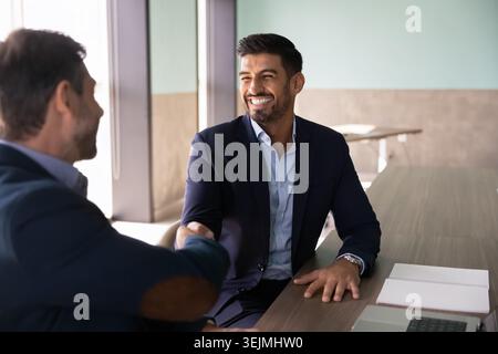 Two businessmen shake hands at conference table in office Stock Photo