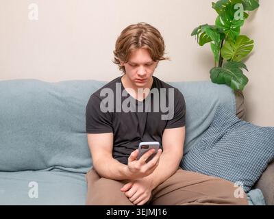 Young man sitting on sofa looking at smartphone at home Stock Photo
