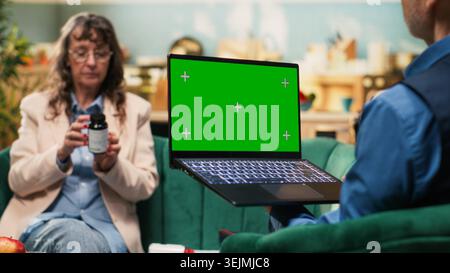 Isolated green screen laptop with two senior people doing their daily healthcare routine, in-home wellbeing during retirement age. Man and woman enjoying free time and longevity, house comfort. Stock Photo