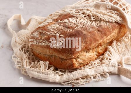 Freshly baked rye bread, ciabatta, in a mesh bag, on a marble light table, natural light, Stock Photo