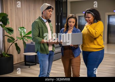Diverse coworkers in casual attire discussing project while reviewing laptop and phone in lounge. Office, coworking, collaborati Stock Photo