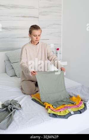 Young woman in comfy clothes arranging clothes sitting on the bed Stock Photo