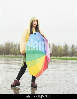 Beautiful brunette woman holding colorful umbrella out in the rain Stock Photo