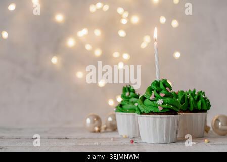 Christmas tree shaped cupcakes, surrounded with festive decorations and lights on the background Stock Photo